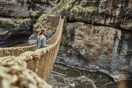 A moment of adventure as a person stands on a suspended bridge over a rugged canyon.