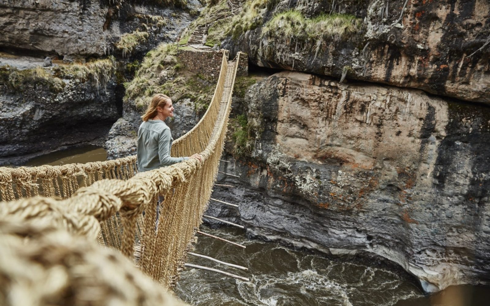 A moment of adventure as a person stands on a suspended bridge over a rugged canyon.